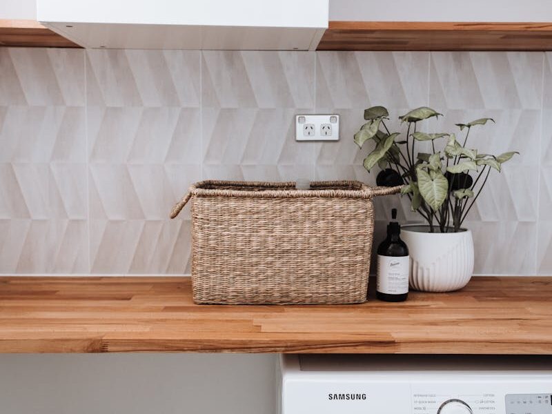 Washing machine under wooden table with plant and wicker basket