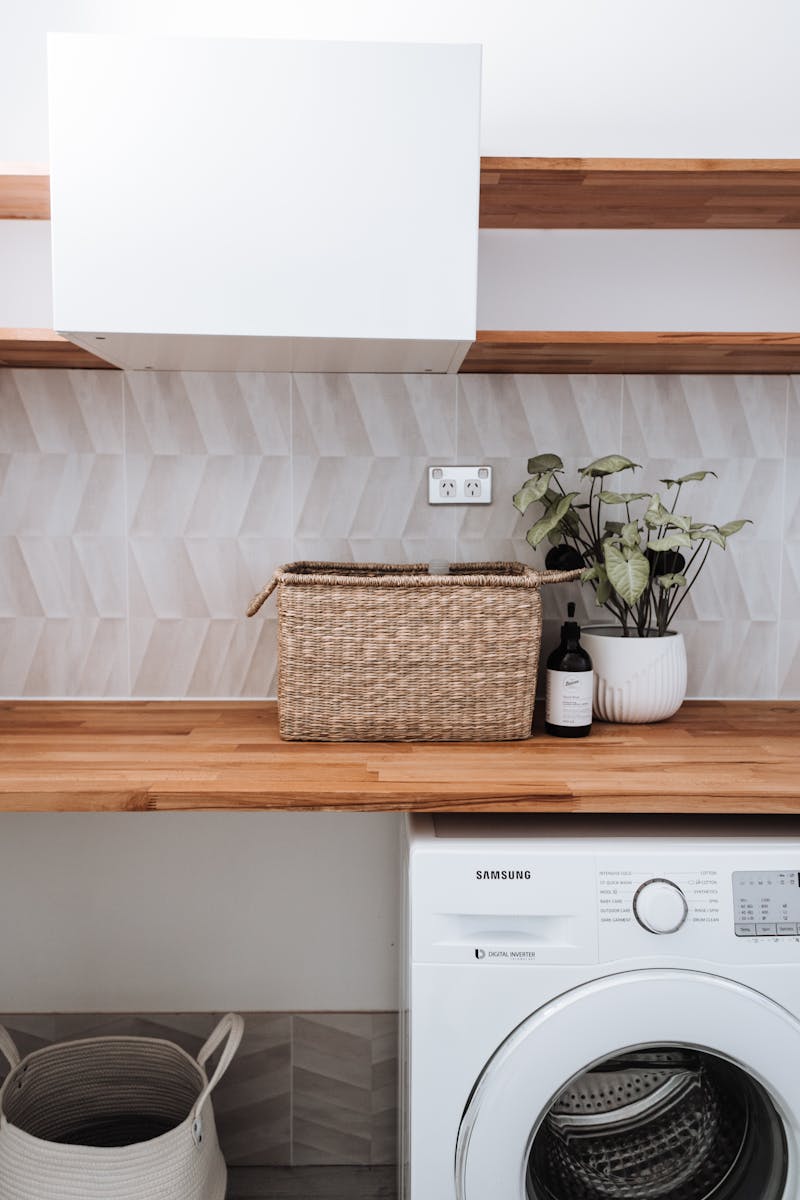 Washing machine under wooden table with plant and wicker basket