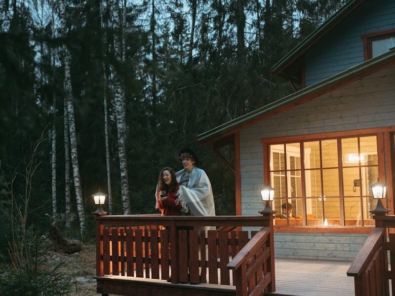 A couple wrapped in a blanket enjoys a winter evening on a forest cabin balcony.