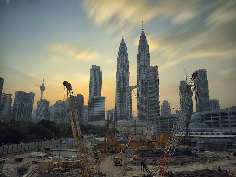 Dramatic view of the Petronas Towers towering over a busy construction site in Kuala Lumpur at sunset.