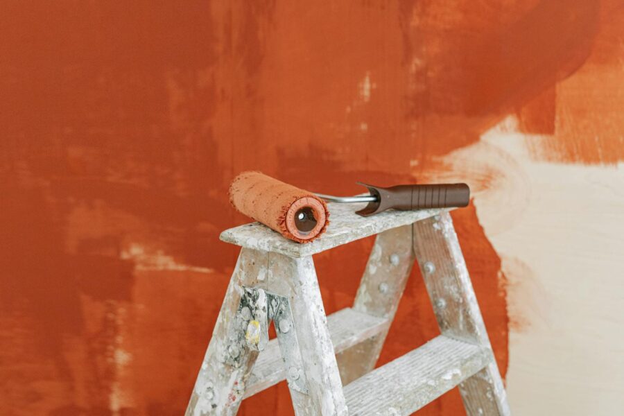 Paint roller on a ladder with a partially painted red wall in the background.