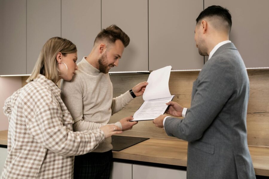 A couple reviews real estate documents with an agent in a modern indoor setting, discussing a potential property purchase.