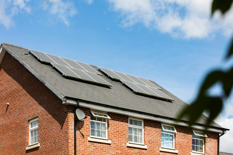 Brick house featuring solar panels on the roof under a clear blue sky, promoting sustainable energy.