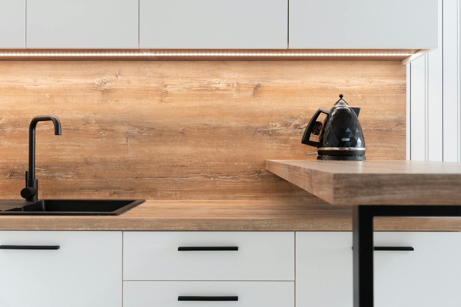 A sleek modern kitchen with wooden backsplash and black kettle, highlighting minimalist design.