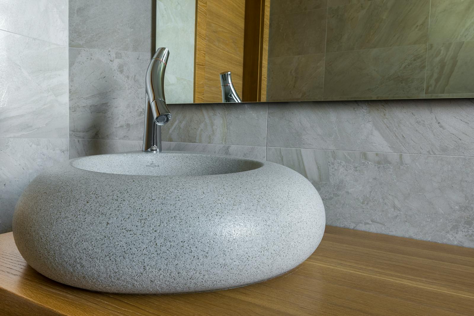 Elegant stone bathroom sink with modern chrome faucet and large mirror.